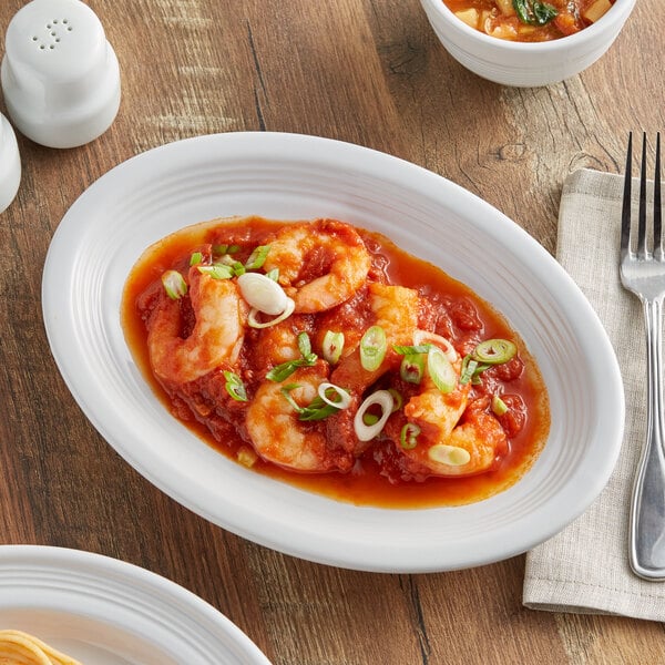 An Acopa Capri oval stoneware platter with shrimp and sauce on a table.