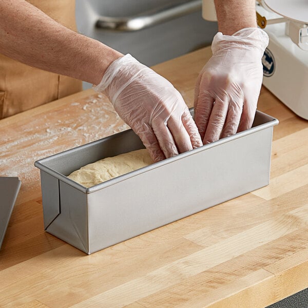 A person in gloves using a Baker's Mark aluminized steel loaf pan to put dough into a loaf
