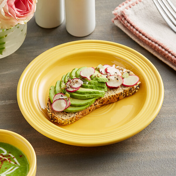 An Acopa Capri citrus yellow stoneware plate with a slice of bread topped with avocado and radish.