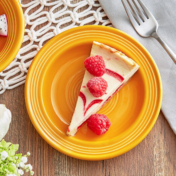A slice of raspberry cheesecake with raspberries on a mango orange Acopa Capri stoneware plate.