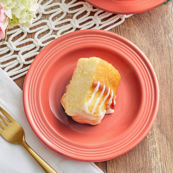 A piece of cake with white frosting on a coral reef stoneware plate with a fork and knife.
