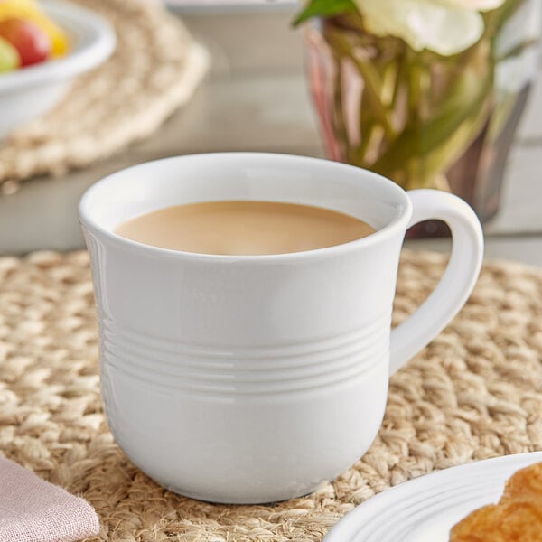 An Acopa Capri white stoneware cup filled with a brown liquid on a table.