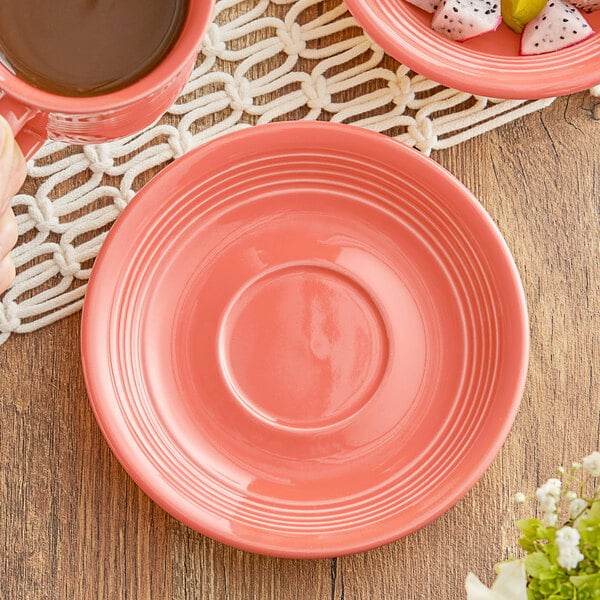 An Acopa Capri coral saucer on a wood table with a cup and flower on it.