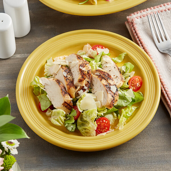 A plate of chicken salad with strawberries, lettuce, and a yellow Acopa Capri stoneware plate on a table.