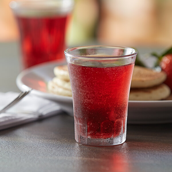 A Duralex Amalfi glass filled with red liquid on a table with food.