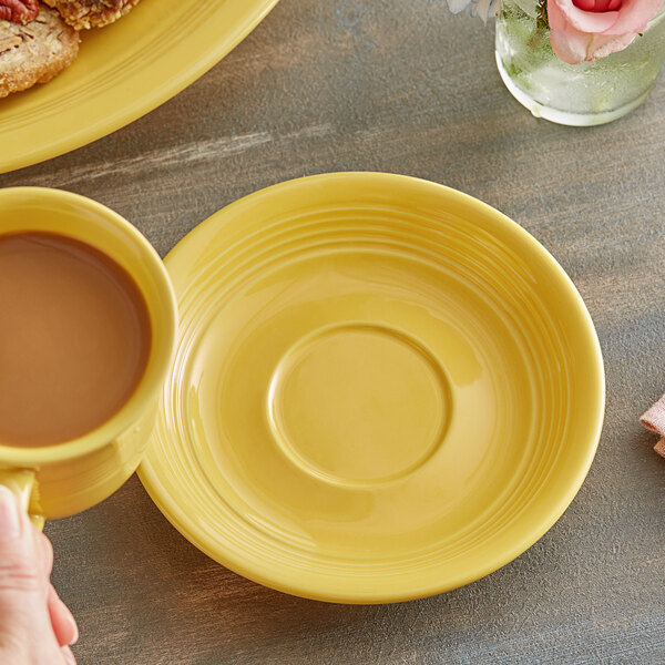 A hand holding a yellow Acopa Capri stoneware saucer with a cup of coffee on it.