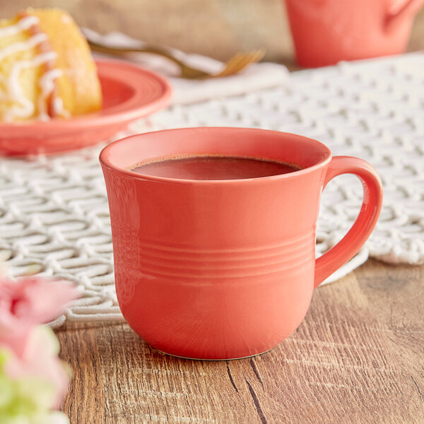 An Acopa Capri coral stoneware cup filled with coffee sitting on a table with pastries.