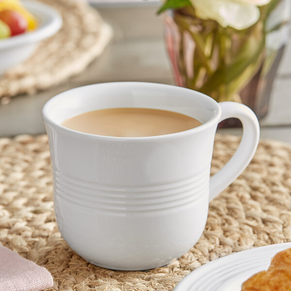 A white Acopa Capri stoneware cup filled with coffee on a white table.