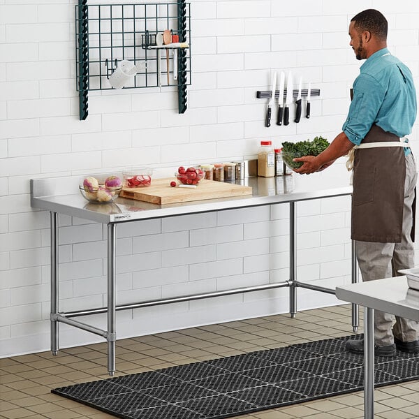 A man standing in a professional kitchen in front of a Regency stainless steel work table.