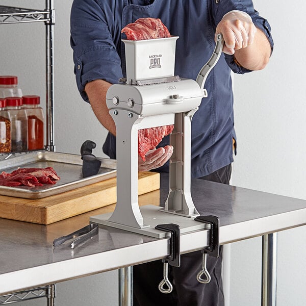 A person using a Backyard Pro manual meat tenderizer on raw meat.