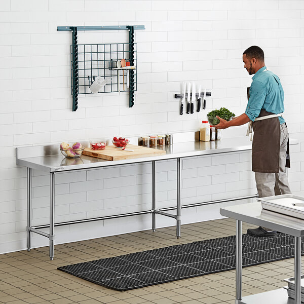 A man standing in a professional kitchen using a Regency stainless steel work table.
