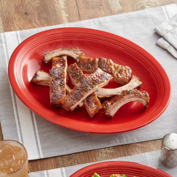 A close up of ribs on a red Acopa Capri stoneware platter.