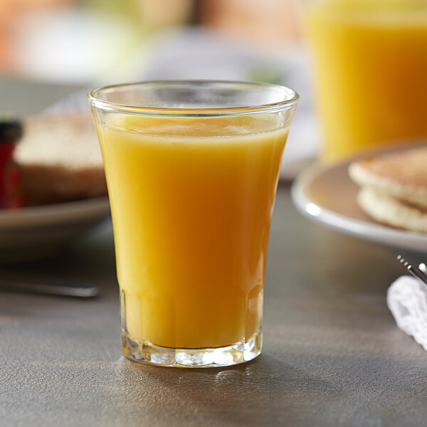 A Duralex glass of orange juice on a table.