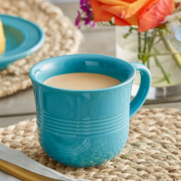 An Acopa Capri Caribbean turquoise stoneware cup filled with a drink on a table with a place mat.