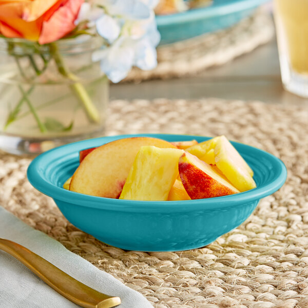 A table with a blue Acopa Capri stoneware bowl filled with fruit on it.
