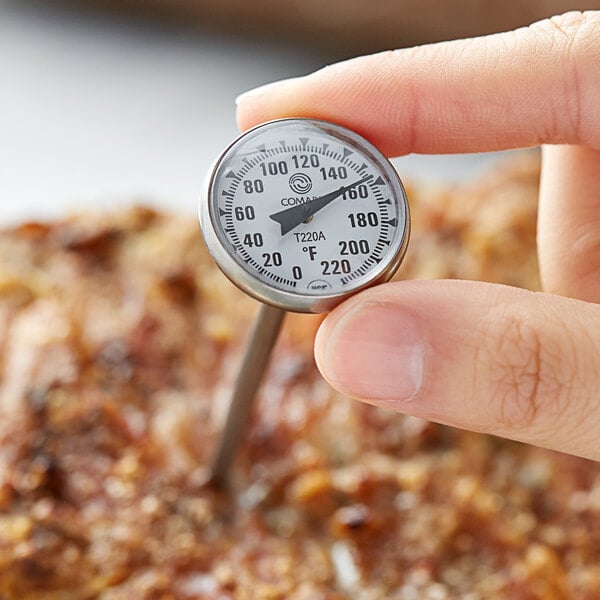 A person holding a Comark pocket probe dial thermometer over a pizza.