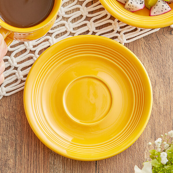 A yellow Acopa Capri stoneware saucer with a cup of coffee on a table.