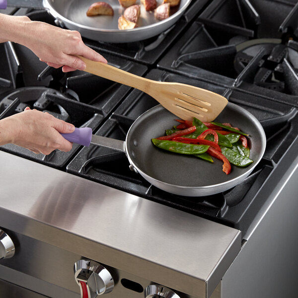 A person cooking vegetables in a Vollrath Wear-Ever non-stick fry pan on a stove.