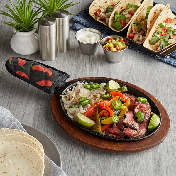A Valor oval cast iron fajita skillet with meat and vegetables on a table.