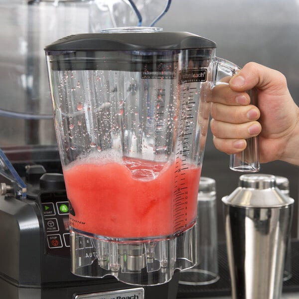 A hand holding a Hamilton Beach blender with a pink smoothie in a clear container.