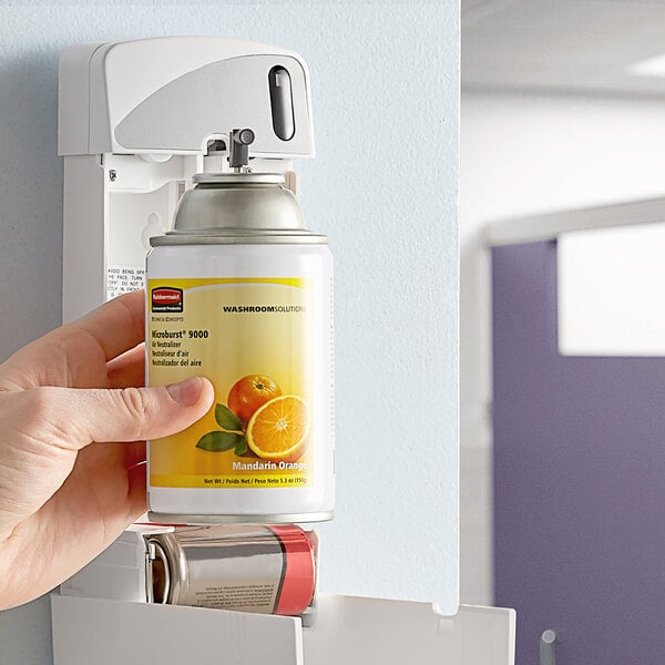 A hand holding a Rubbermaid Microburst 9000 air freshener can with an orange label.