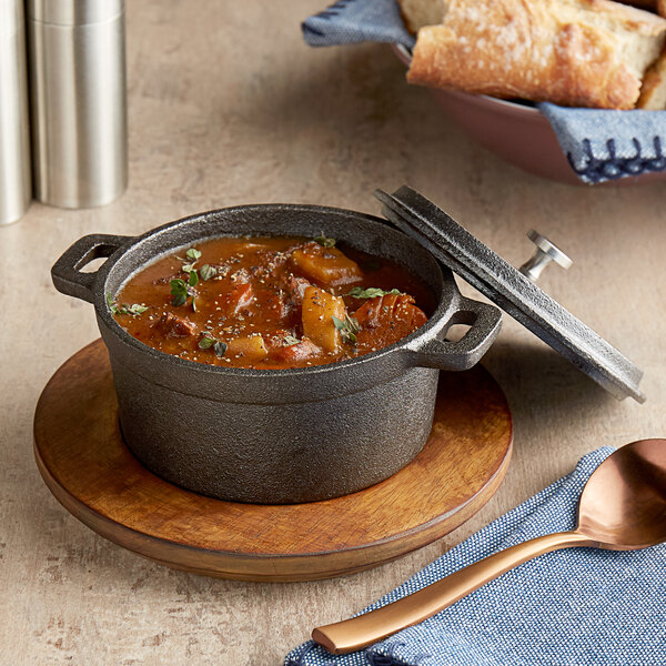 A Valor pre-seasoned cast iron pot of soup on a wooden plate with a spoon and bread.