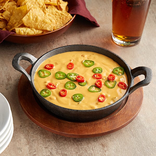 A Valor pre-seasoned cast iron casserole dish with chili cheese dip and chips on a table with a glass of beer.
