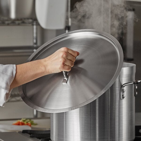 A person using a Vollrath stainless steel domed lid on a pot.