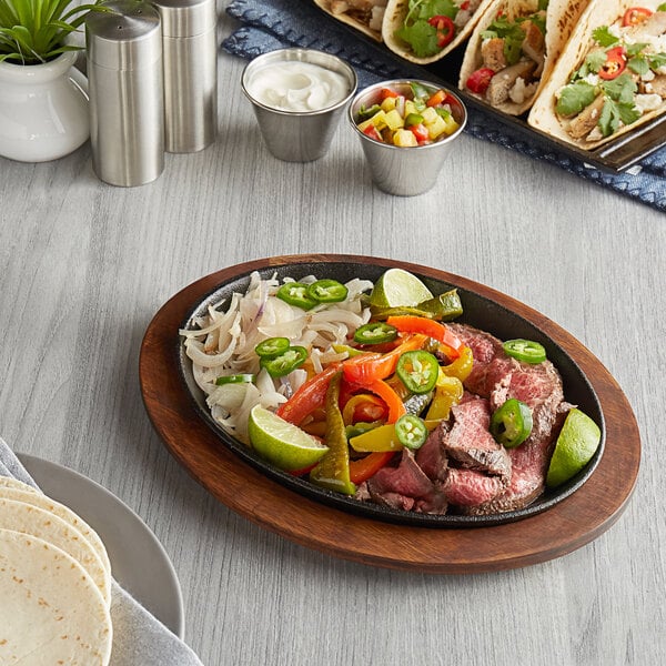 A Valor oval cast iron fajita skillet with meat, vegetables, and tortillas on a wood table.