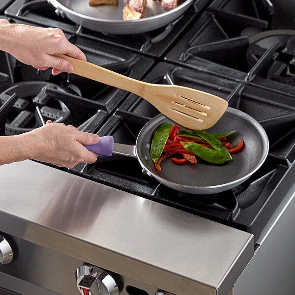 A person cooking food in a Vollrath purple-handled fry pan on a stove top.
