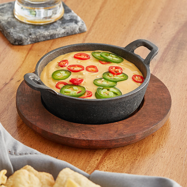 A Valor pre-seasoned cast iron bowl of chili cheese dip on a wood table with a wooden underliner.