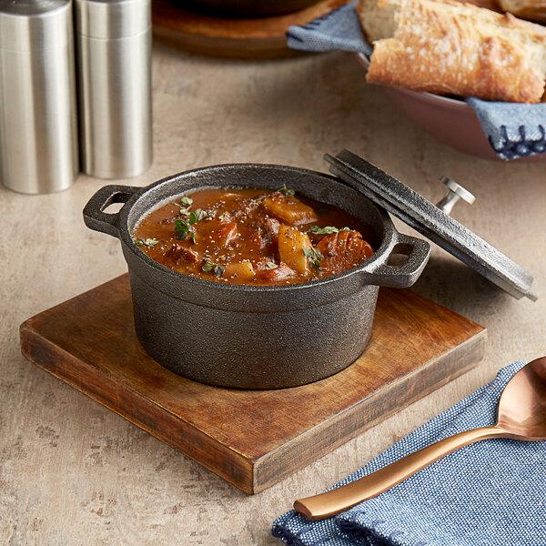 A Valor pre-seasoned cast iron pot of stew on a wood board with bread and a spoon.