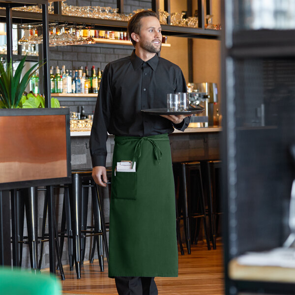 A man wearing a Choice hunter green bistro apron holding a tray.
