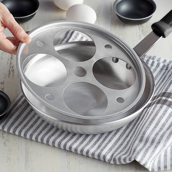 A hand holding a Vollrath aluminum pan with holes in it.