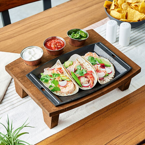 A rectangular cast iron skillet with shrimp tacos and vegetables on a table.