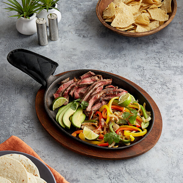 A Valor oval cast iron fajita skillet with meat and vegetables on it, with tortillas and a bowl of chips.