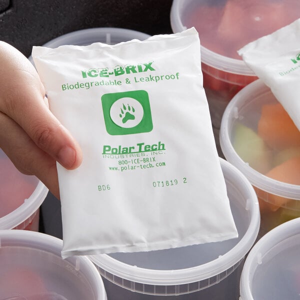 A hand holding a white plastic container filled with Polar Tech Biodegradable Ice Brix