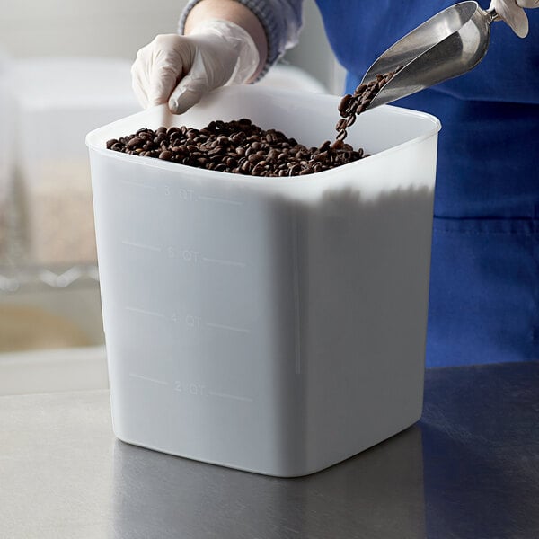 A person pouring coffee beans into a white Carlisle food storage container.