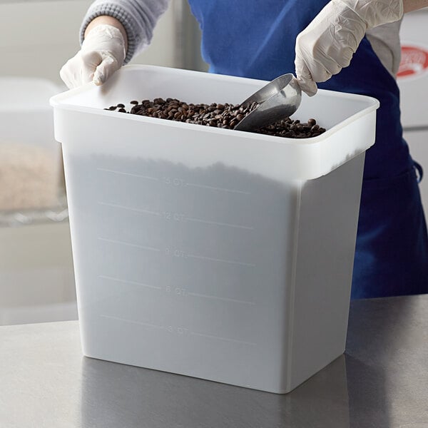 A person in gloves pouring coffee beans into a white Carlisle food storage container.