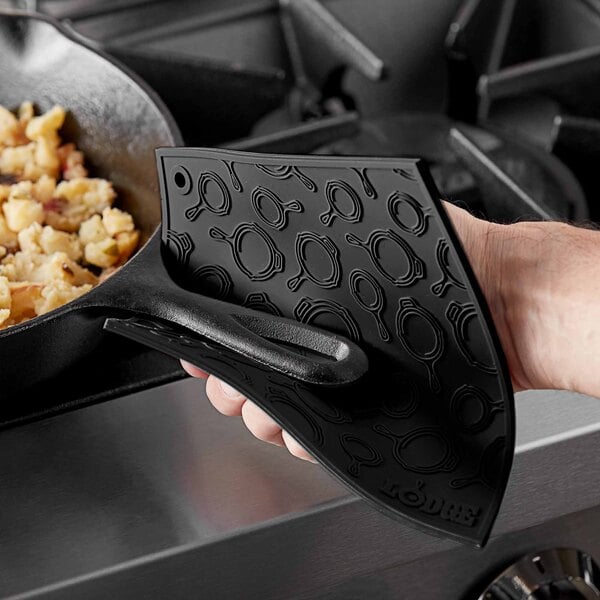 A hand holding a Lodge black silicone spatula over a black skillet with food.