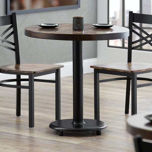 A Lancaster Table & Seating cast iron table base with a black finish on a round table with two chairs.