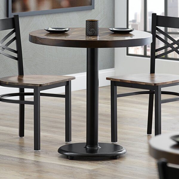 A Lancaster Table & Seating cast iron table base with two chairs at a restaurant table.