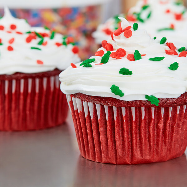 A close-up of a red cupcake in a white Hoffmaster fluted wrapper with white frosting and sprinkles.