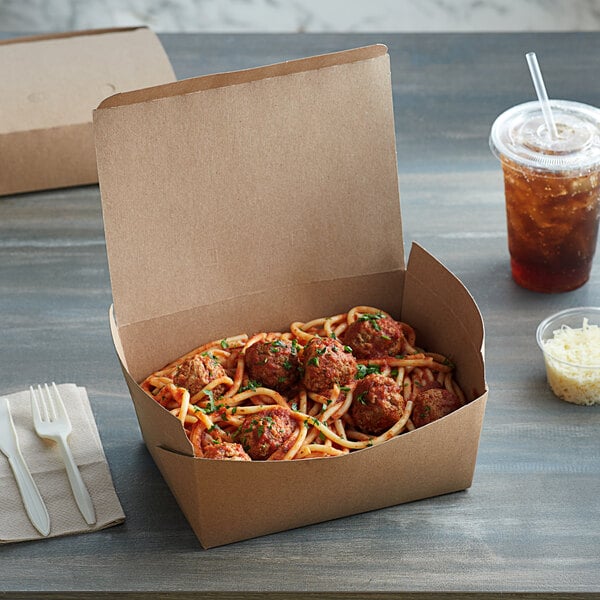 A Fold-Pak Bio-Plus Dine take-out container with spaghetti and meatballs inside on a table with a plastic cup of brown liquid and a straw.