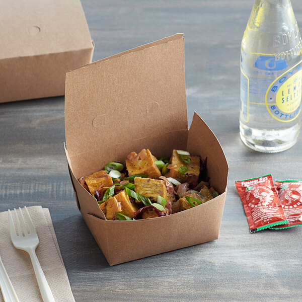 A Kraft Fold-Pak take-out box of food with a lid on a table.