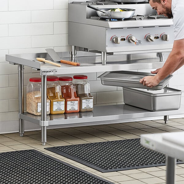 A man using a Regency stainless steel equipment stand in a professional kitchen.