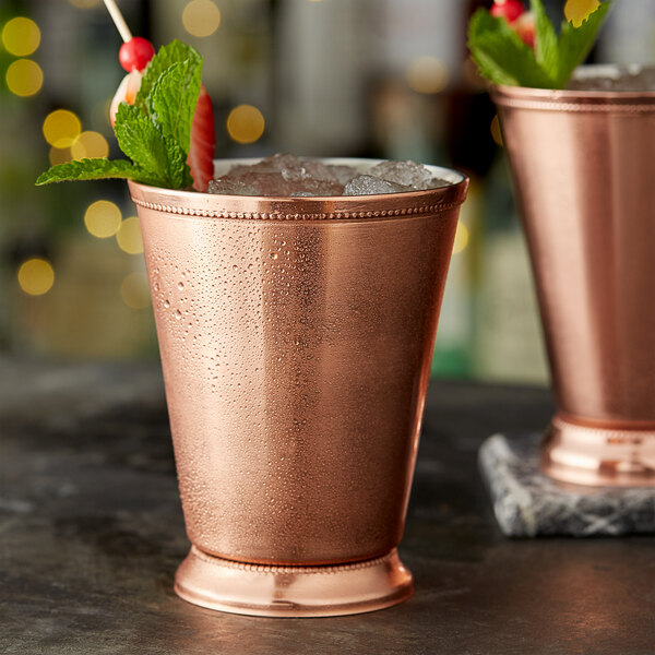 A close up of an Acopa copper mint julep cup filled with ice and mint leaves.