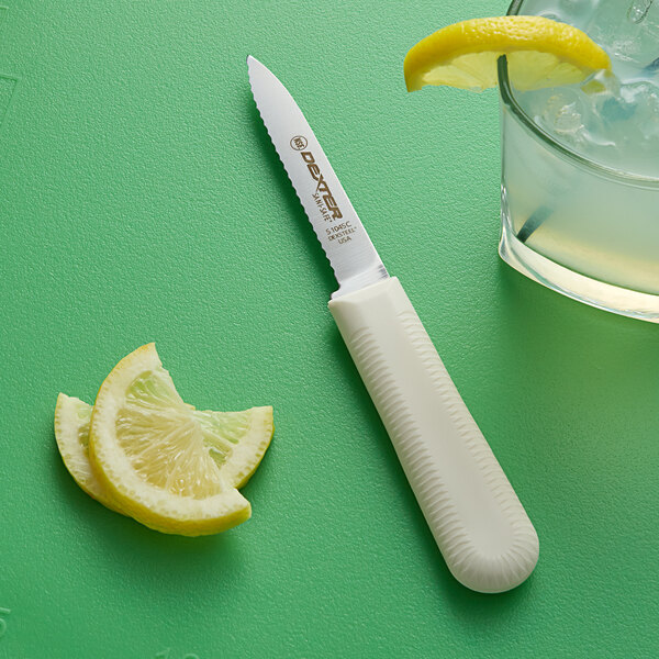 A Dexter-Russell scalloped paring knife next to lemon slices on a green surface.
