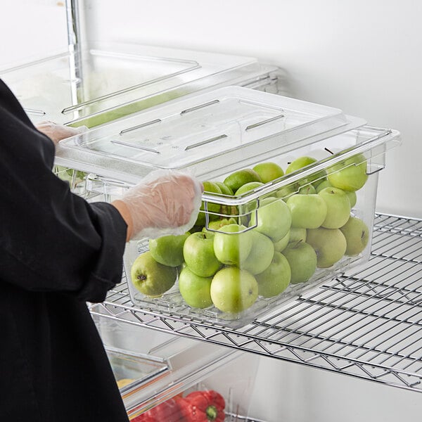 A person putting green apples in a Cambro clear food storage container.