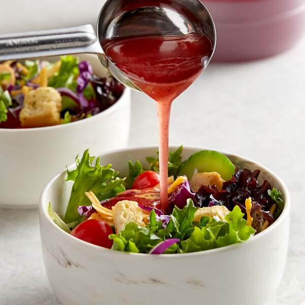A pink bowl of salad with Ken's red wine vinegar and oil dressing being poured on it.